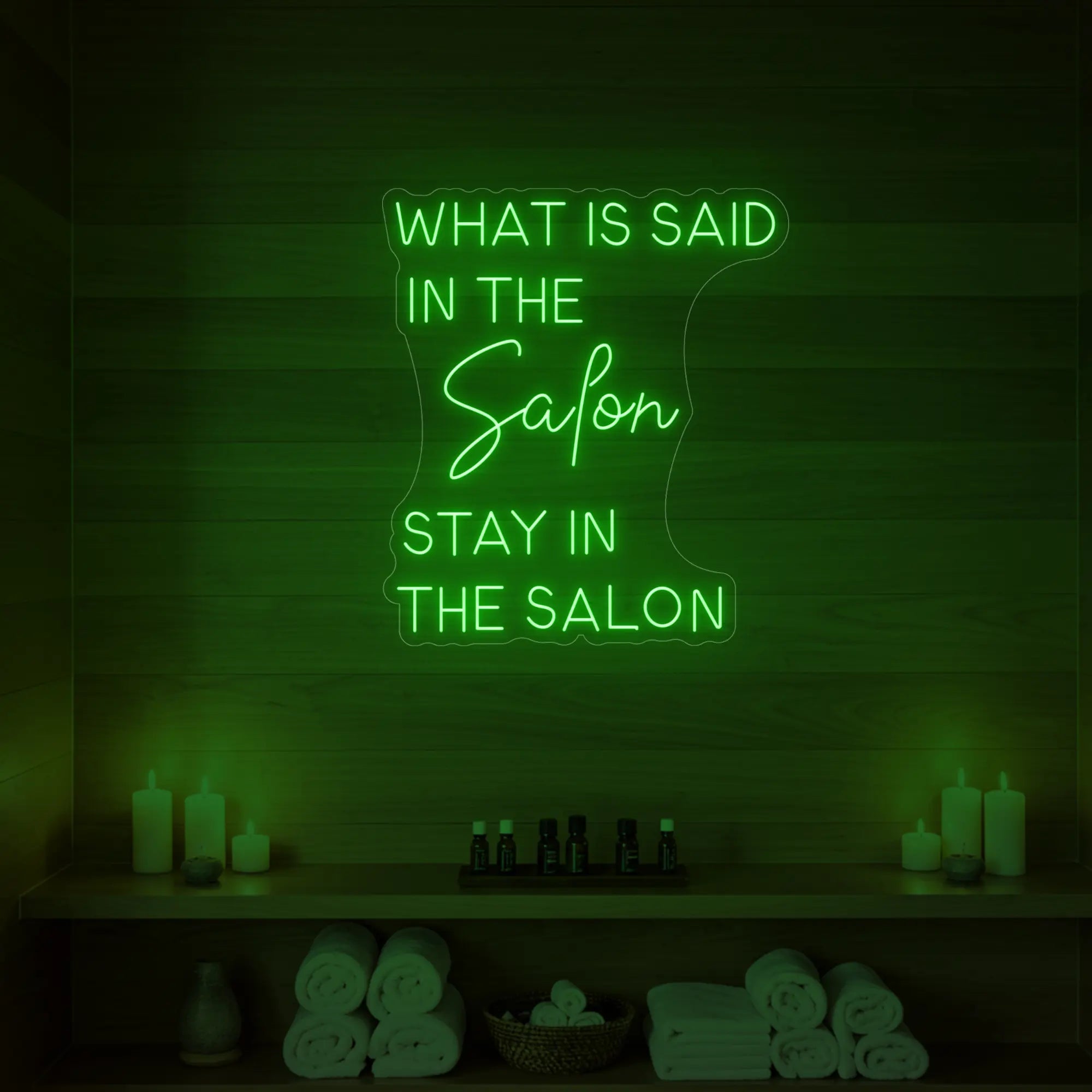 Photo of the 'WHAT IS SAID IN THE SALON STAY IN THE SALON' neon sign glowing in green against a styled interior wall.