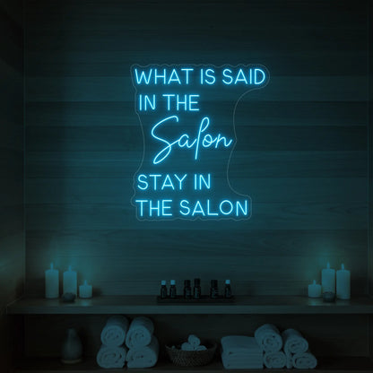 Photo of the 'WHAT IS SAID IN THE SALON STAY IN THE SALON' neon sign glowing in ice blue against a styled interior wall.