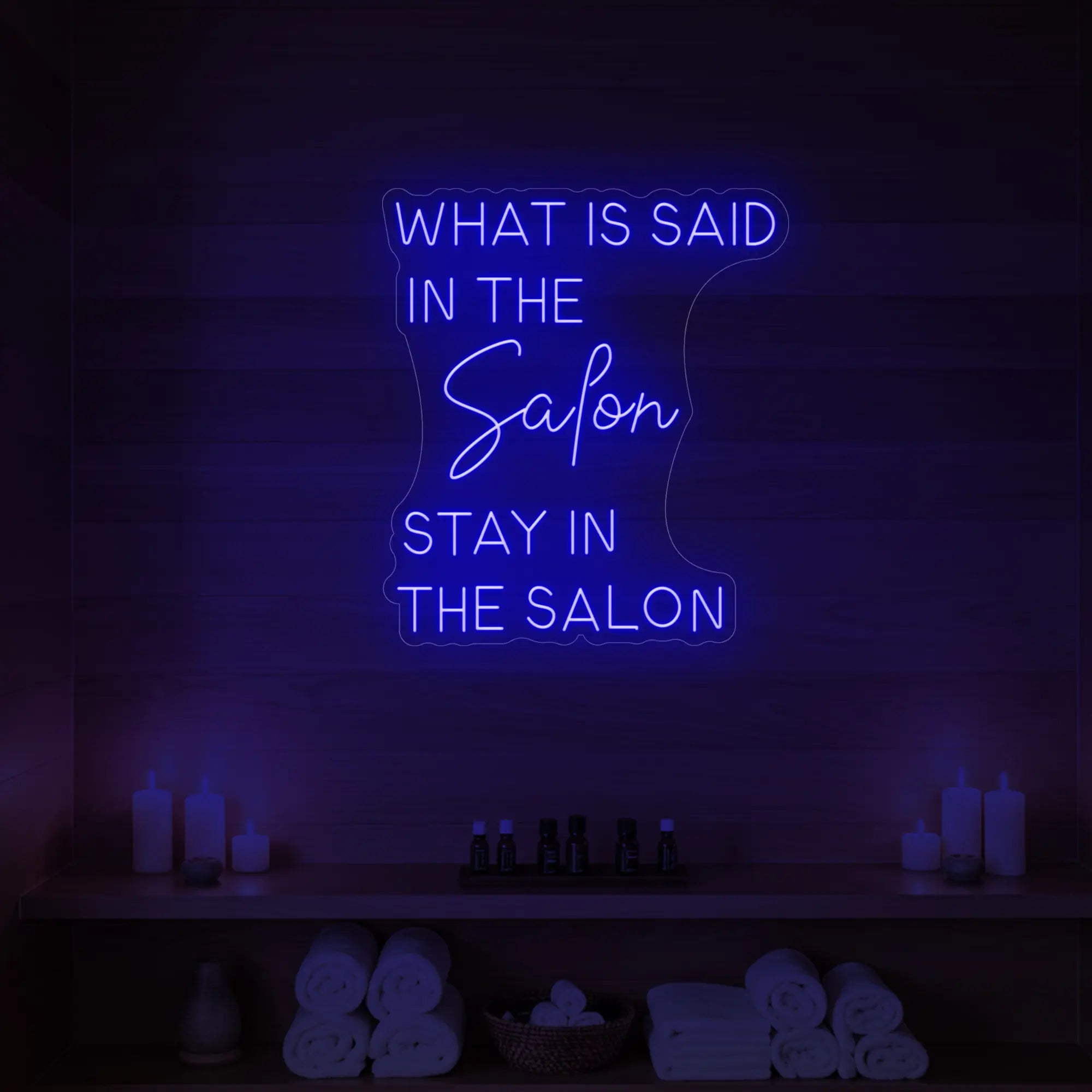 Photo of the 'WHAT IS SAID IN THE SALON STAY IN THE SALON' neon sign glowing in deep blue against a styled interior wall.