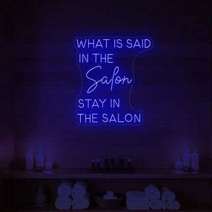 Photo of the 'WHAT IS SAID IN THE SALON STAY IN THE SALON' neon sign glowing in deep blue against a styled interior wall.