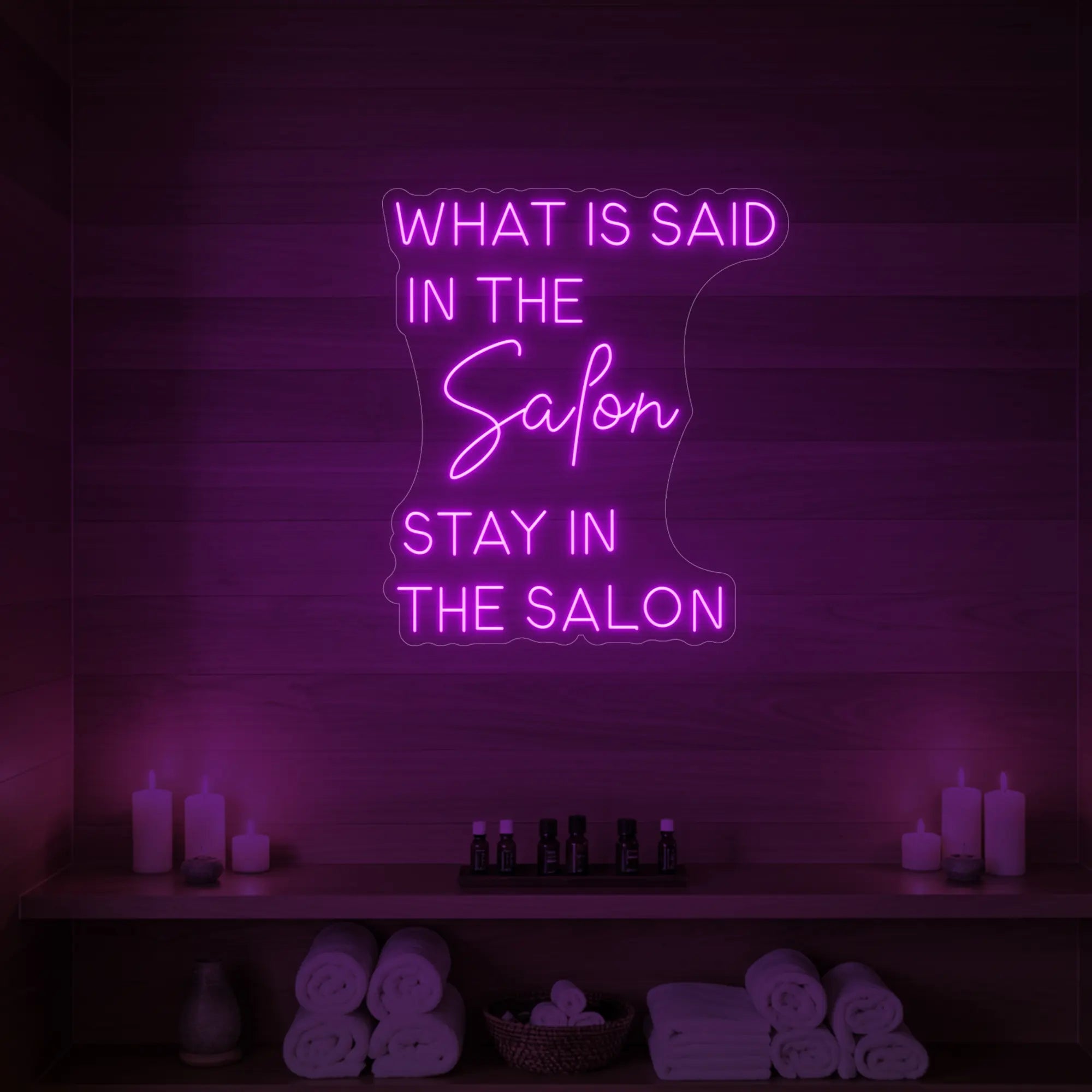 Photo of the 'WHAT IS SAID IN THE SALON STAY IN THE SALON' neon sign glowing in deep pink against a styled interior wall.