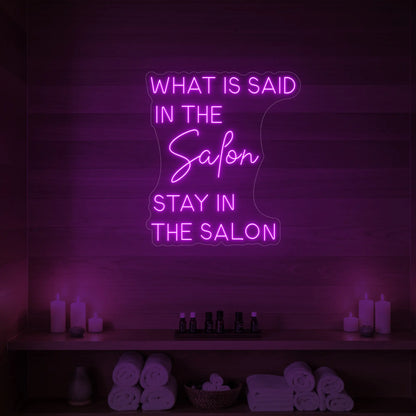 Photo of the 'WHAT IS SAID IN THE SALON STAY IN THE SALON' neon sign glowing in deep pink against a styled interior wall.