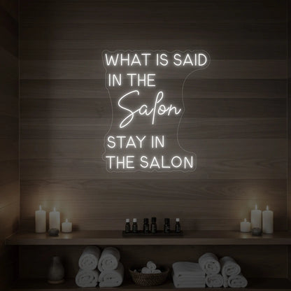 Photo of the 'WHAT IS SAID IN THE SALON STAY IN THE SALON' neon sign glowing in cool white against a styled interior wall.