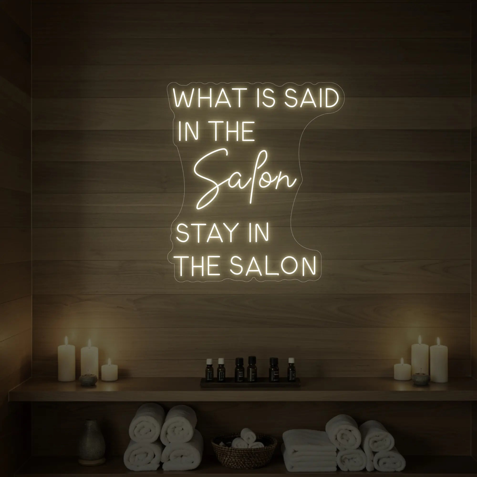 Photo of the 'WHAT IS SAID IN THE SALON STAY IN THE SALON' neon sign glowing in warm white against a styled interior wall.