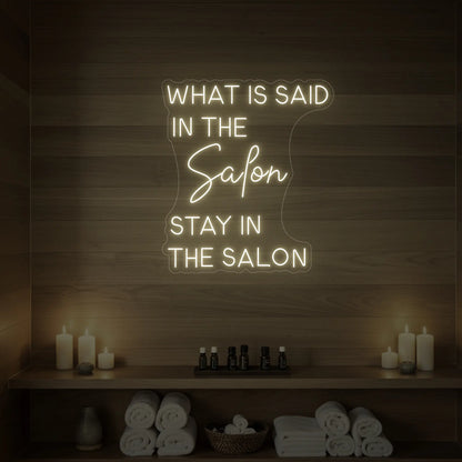 Photo of the 'WHAT IS SAID IN THE SALON STAY IN THE SALON' neon sign glowing in warm white against a styled interior wall.