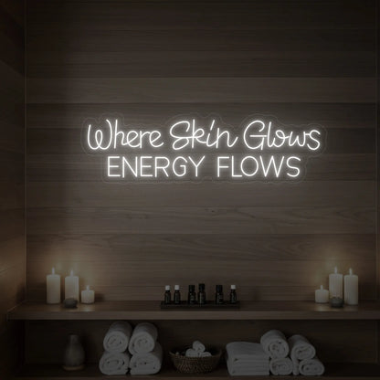 Photo of the 'Where Skin Glows, Energy Flows' neon sign glowing in cool white against a styled interior wall.