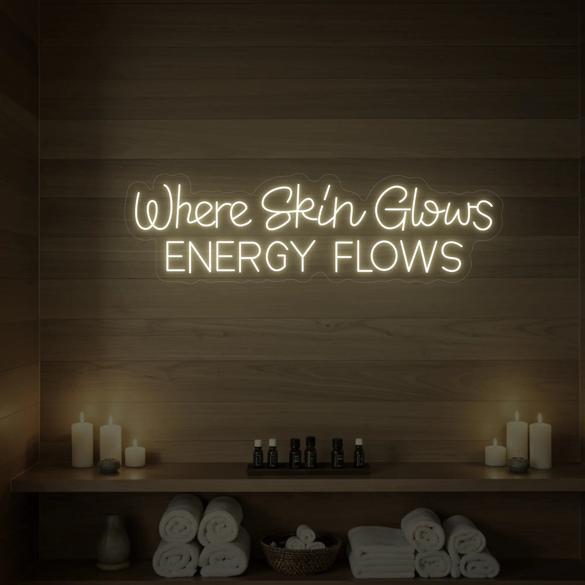 Photo of the 'Where Skin Glows, Energy Flows' neon sign glowing in warm white against a styled interior wall.