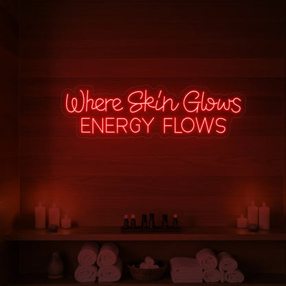 Photo of the 'Where Skin Glows, Energy Flows' neon sign glowing in red against a styled interior wall.