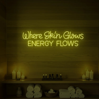 Photo of the 'Where Skin Glows, Energy Flows' neon sign glowing in lemon yellow against a styled interior wall.