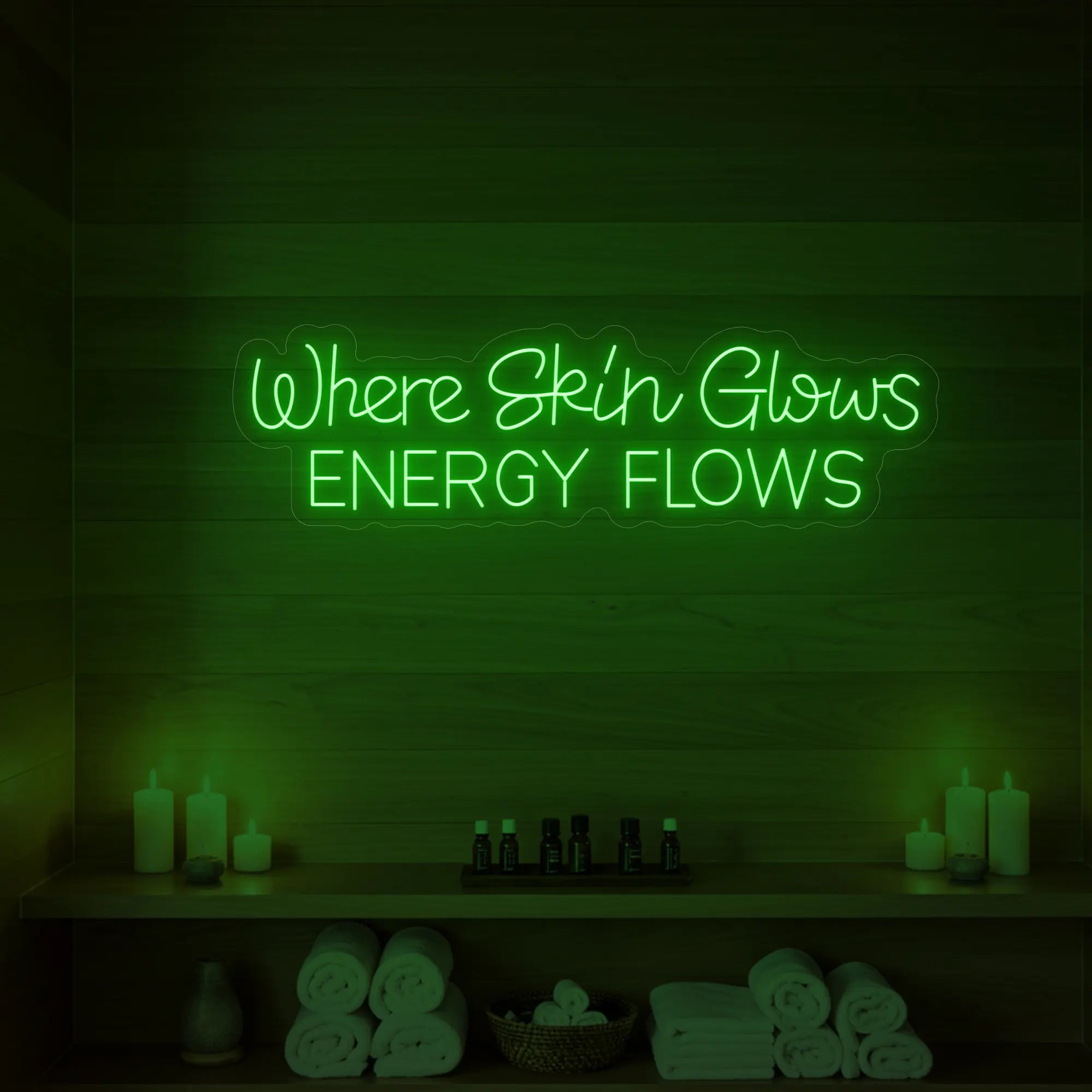 Photo of the 'Where Skin Glows, Energy Flows' neon sign glowing in green against a styled interior wall.