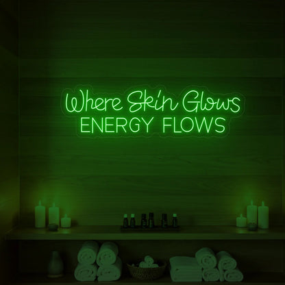 Photo of the 'Where Skin Glows, Energy Flows' neon sign glowing in green against a styled interior wall.