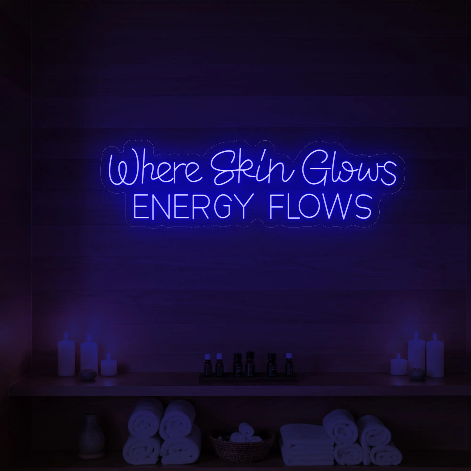 Photo of the 'Where Skin Glows, Energy Flows' neon sign glowing in deep blue against a styled interior wall.