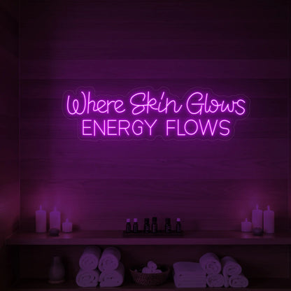 Photo of the 'Where Skin Glows, Energy Flows' neon sign glowing in deep pink against a styled interior wall.