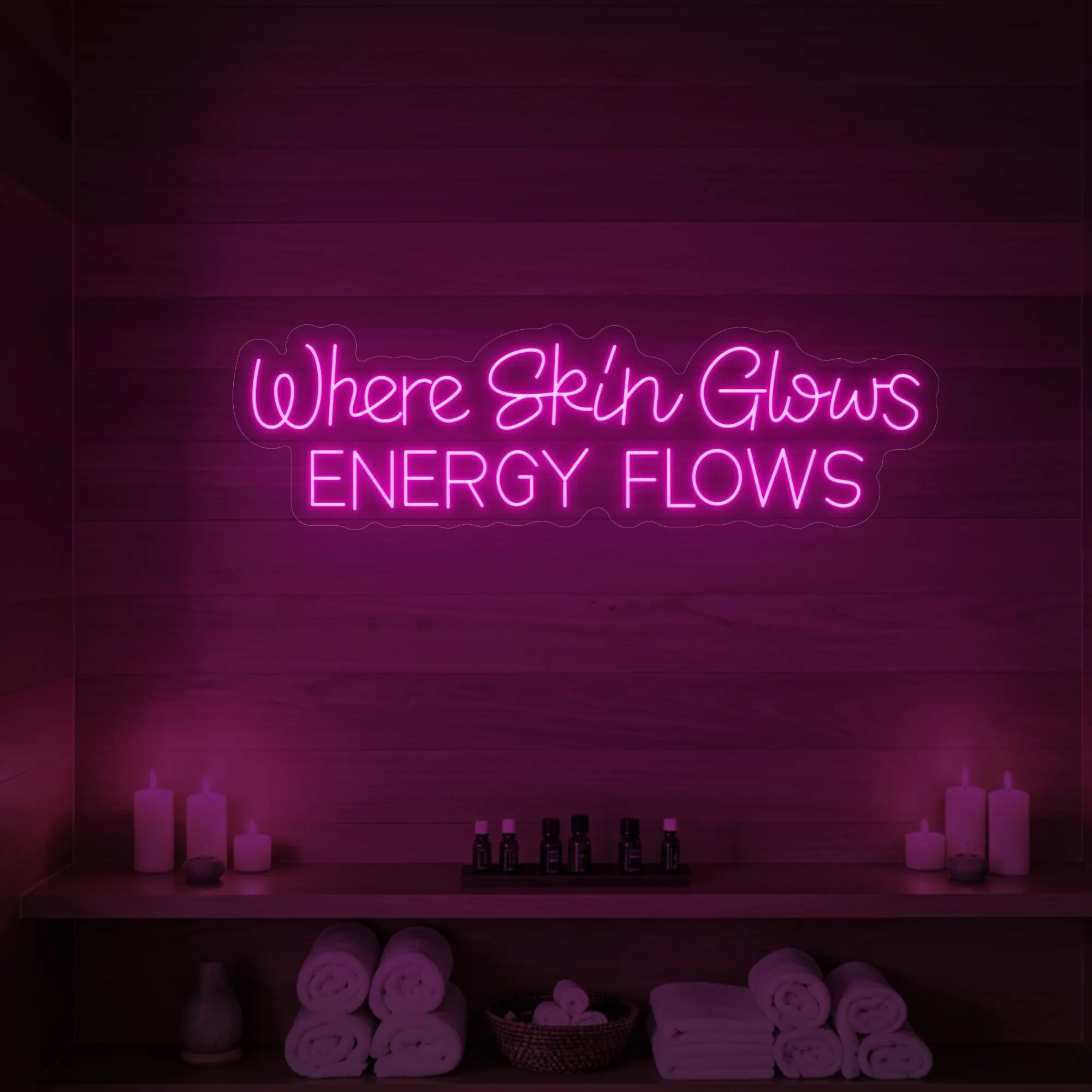 Photo of the 'Where Skin Glows, Energy Flows' neon sign glowing in light pink against a styled interior wall.