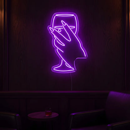 Photo of the 'Wine in Hand Version 1' neon sign glowing in purple against a cozy wine-inspired wall.