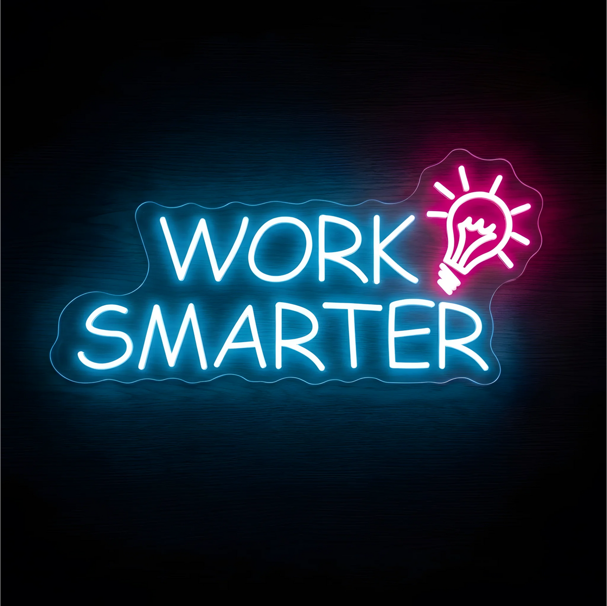 Work Smarter LED Neon Sign with white uppercase lettering and a pink light bulb icon with radiating lines on clear acrylic against a dark wood background, suited to offices and creative studios.