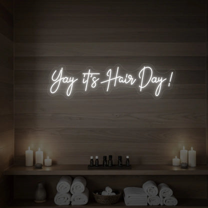 Photo of the 'Yay it’s Hair Day!' neon sign glowing in cool white against a styled interior wall.