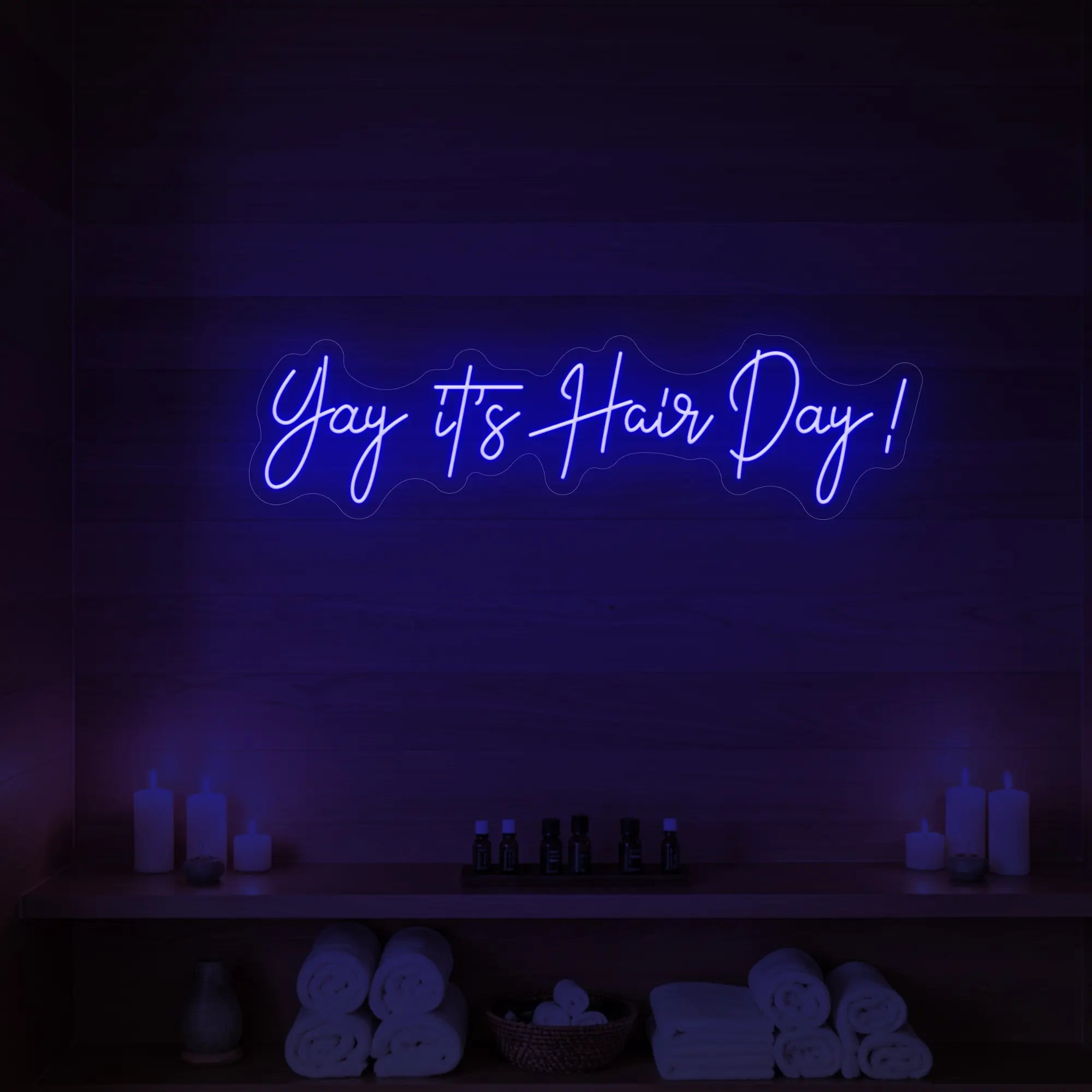 Photo of the 'Yay it’s Hair Day!' neon sign glowing in deep blue against a styled interior wall.