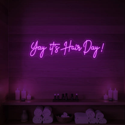 Photo of the 'Yay it’s Hair Day!' neon sign glowing in deep pink against a styled interior wall.