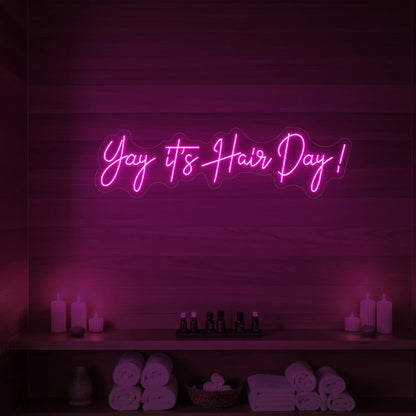 Photo of the 'Yay it’s Hair Day!' neon sign glowing in light pink against a styled interior wall.