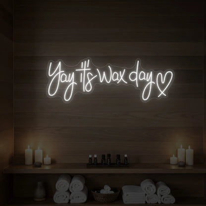 Photo of the 'Yay It’s Wax Day ❤' neon sign glowing in cool white against a styled interior wall.