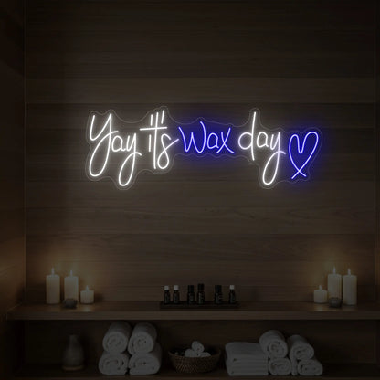 Photo of the 'Yay It’s Wax Day ❤' neon sign glowing in deep blue against a styled interior wall.