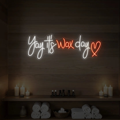 Photo of the 'Yay It’s Wax Day ❤' neon sign glowing in golden yellow against a styled interior wall.