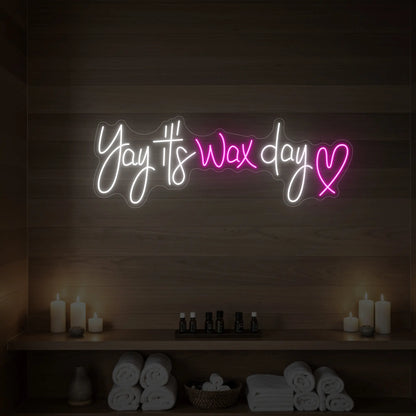 Photo of the 'Yay It’s Wax Day ❤' neon sign glowing in light pink against a styled interior wall.