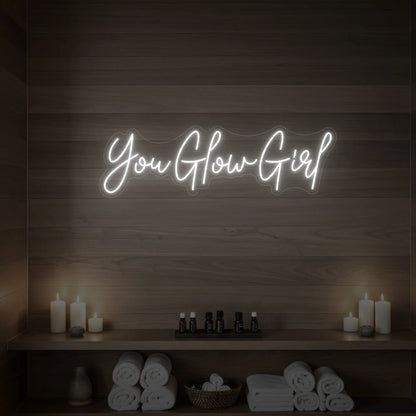 Photo of the 'You Glow Girl' neon sign glowing in cool white against a styled interior wall.