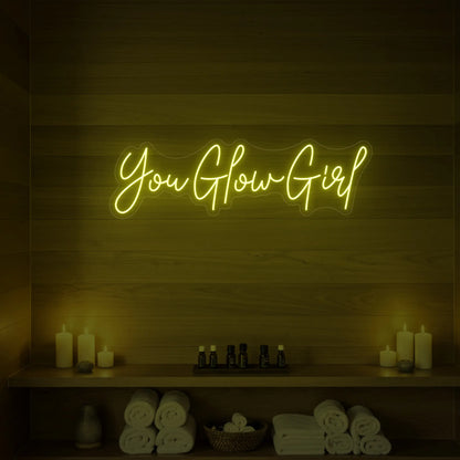 Photo of the 'You Glow Girl' neon sign glowing in lemon yellow against a styled interior wall.