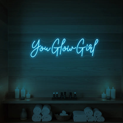 Photo of the 'You Glow Girl' neon sign glowing in ice blue against a styled interior wall.