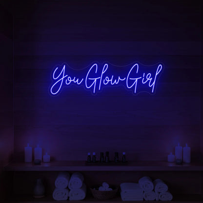 Photo of the 'You Glow Girl' neon sign glowing in deep blue against a styled interior wall.