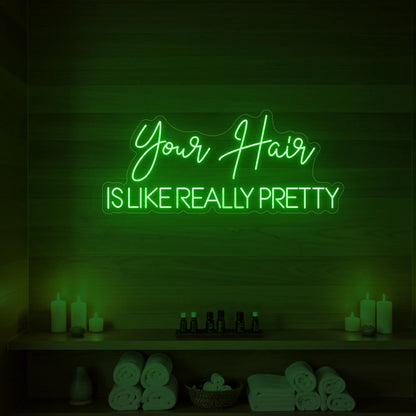 Photo of the 'Your Hair Is Like Really Pretty' neon sign glowing in green against a styled interior wall.