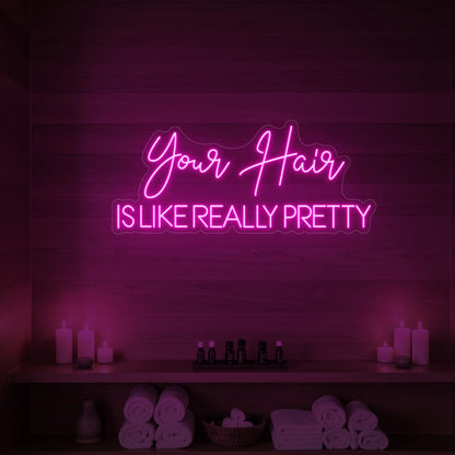 Photo of the 'Your Hair Is Like Really Pretty' neon sign glowing in light pink against a styled interior wall.