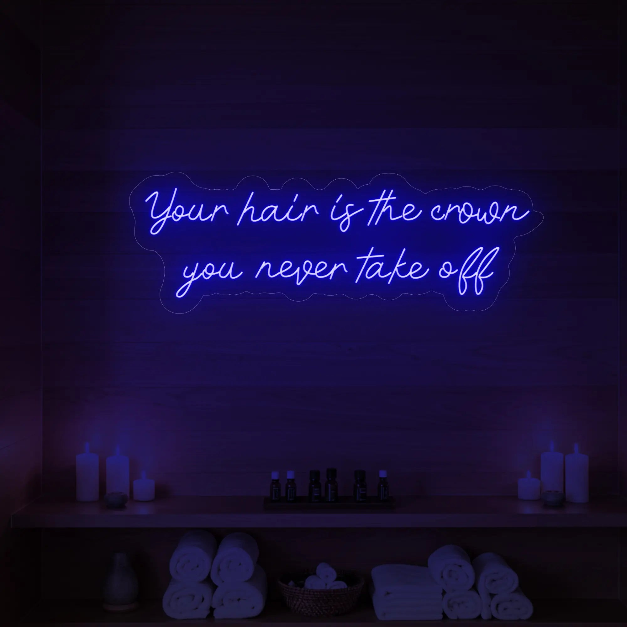 Photo of the 'Your Hair Is The Crown You Never Take Off' neon sign glowing in deep blue against a styled interior wall.