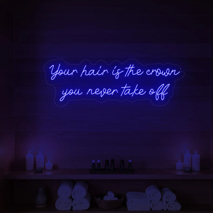 Photo of the 'Your Hair Is The Crown You Never Take Off' neon sign glowing in deep blue against a styled interior wall.