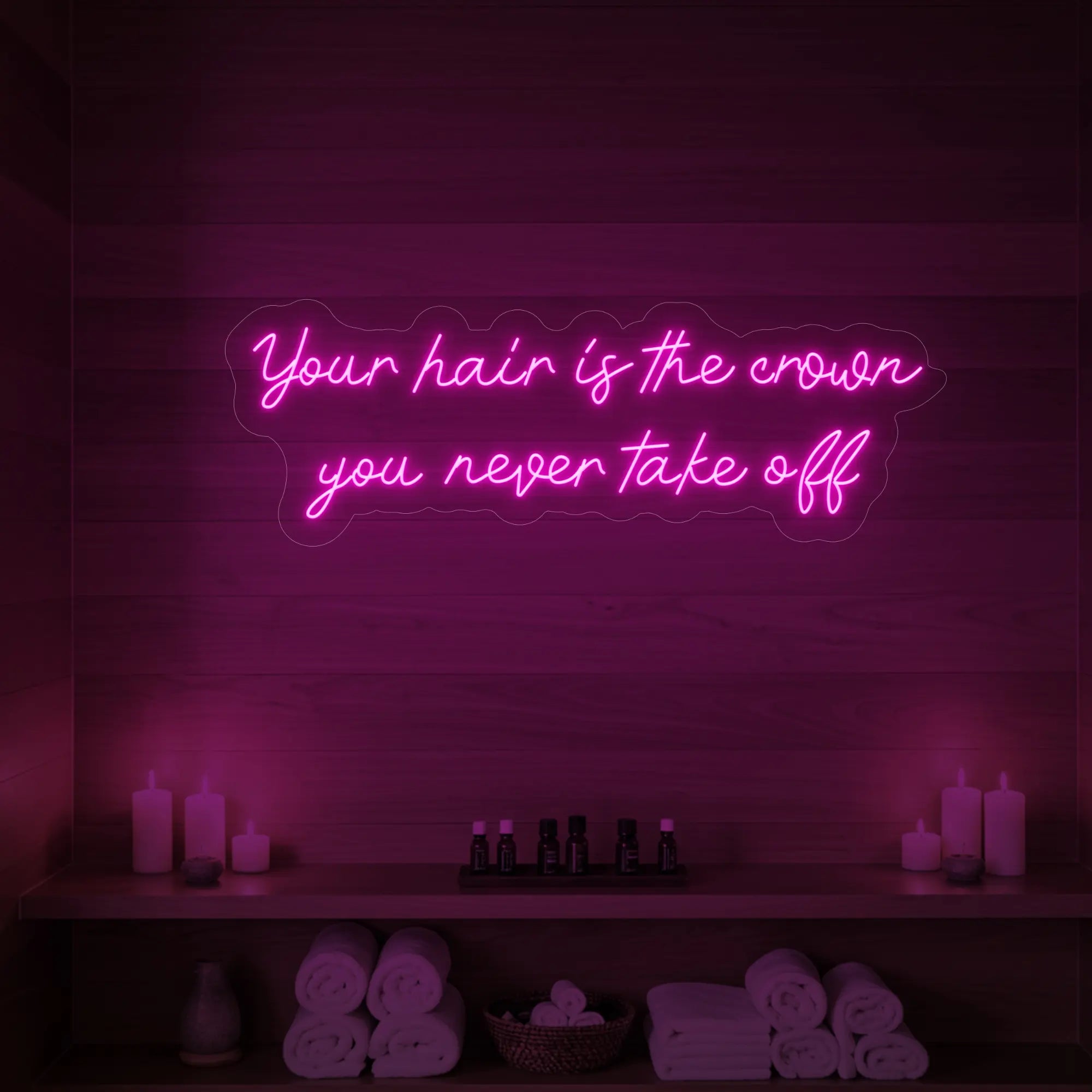 Photo of the 'Your Hair Is The Crown You Never Take Off' neon sign glowing in light pink against a styled interior wall.