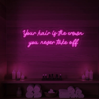 Photo of the 'Your Hair Is The Crown You Never Take Off' neon sign glowing in light pink against a styled interior wall.