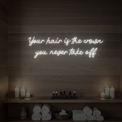 Photo of the 'Your Hair Is The Crown You Never Take Off' neon sign glowing in cool white against a styled interior wall.