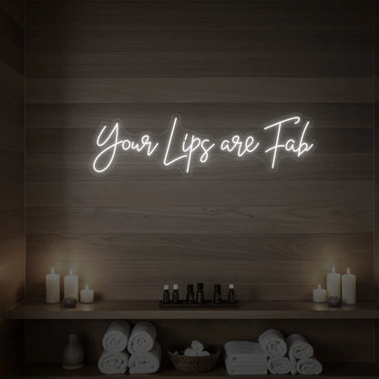 Photo of the 'Your Lips Are Fab' neon sign glowing in cool white against a styled interior wall.