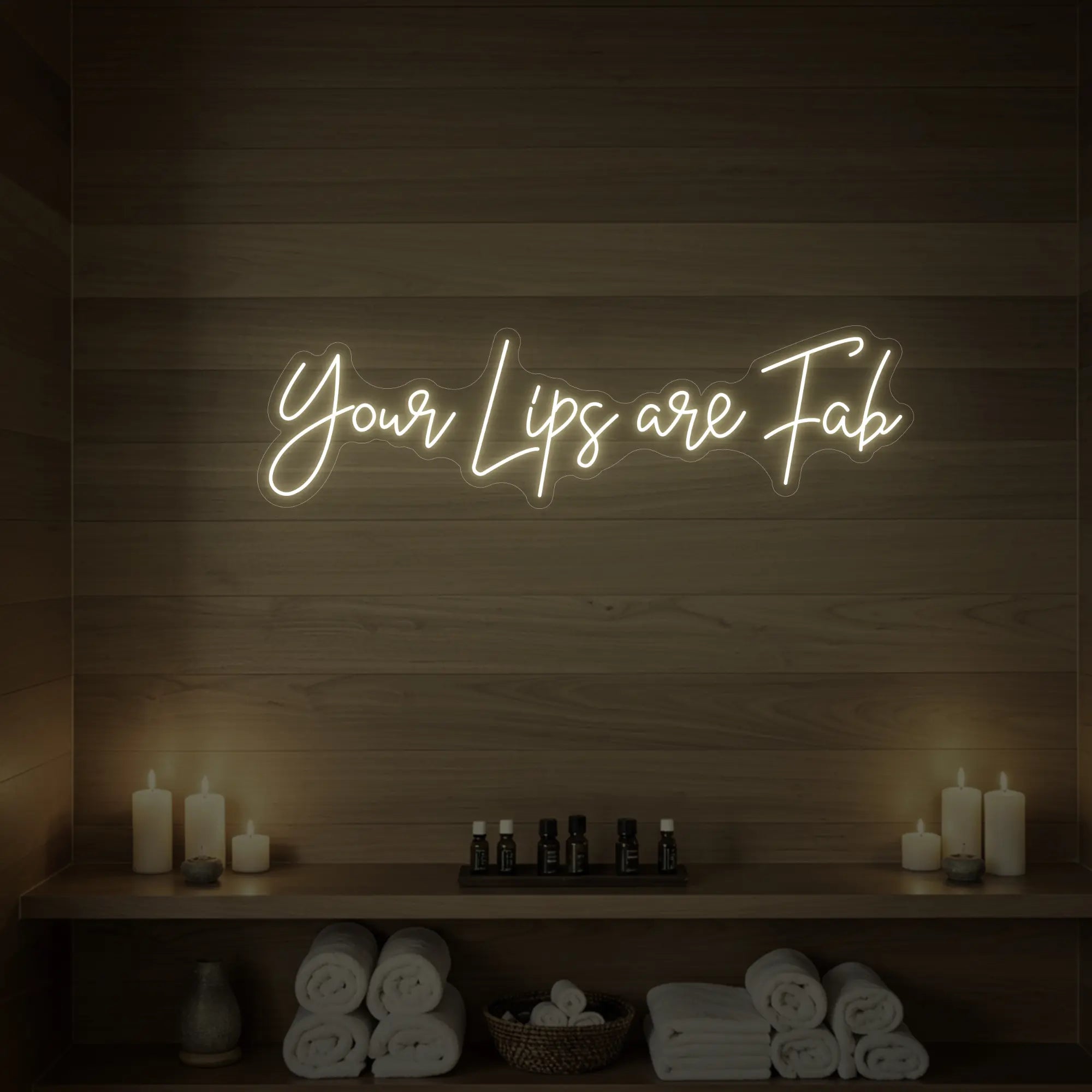 Photo of the 'Your Lips Are Fab' neon sign glowing in warm white against a styled interior wall.