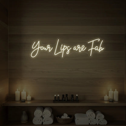 Photo of the 'Your Lips Are Fab' neon sign glowing in warm white against a styled interior wall.