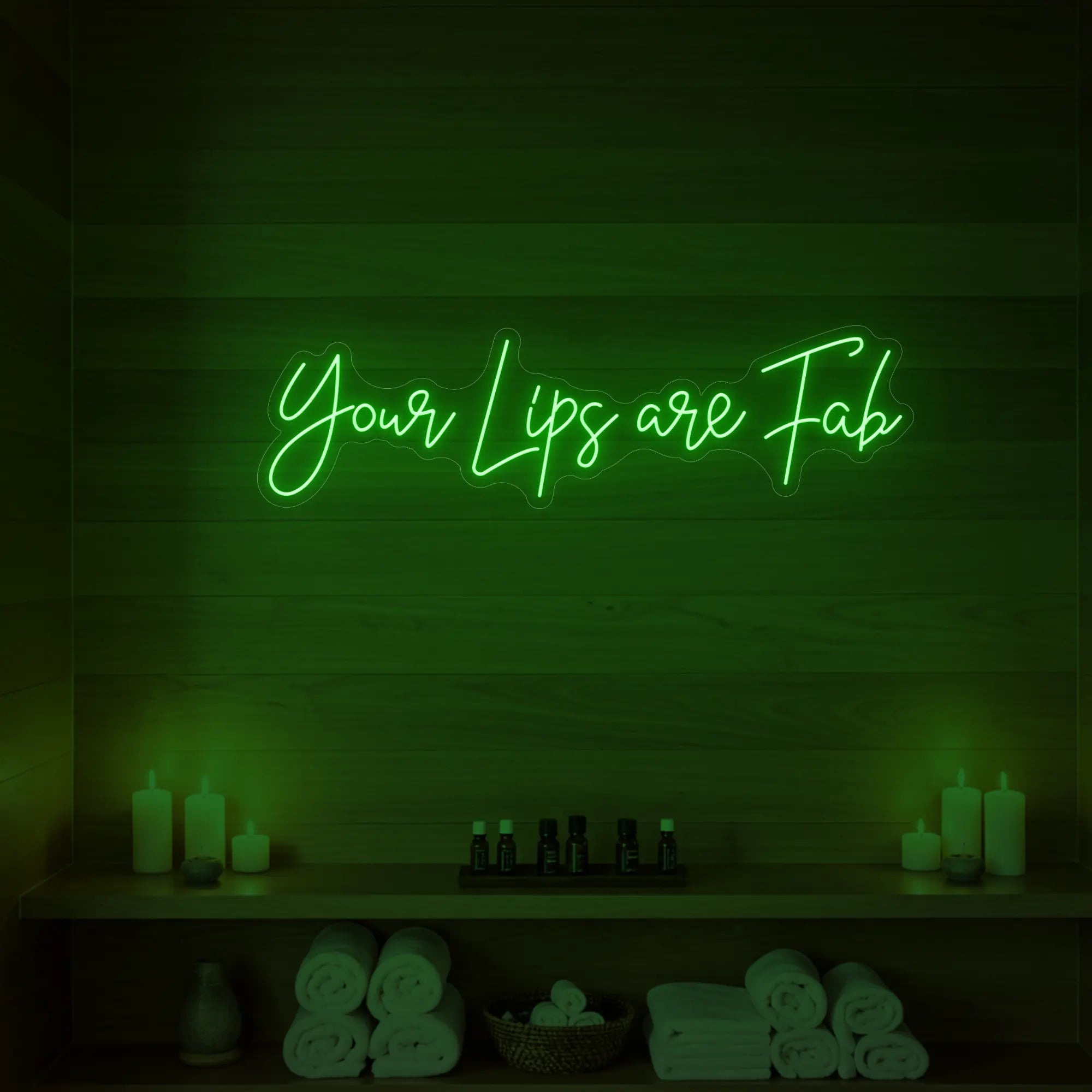 Photo of the 'Your Lips Are Fab' neon sign glowing in green against a styled interior wall.