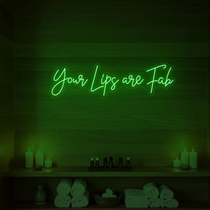 Photo of the 'Your Lips Are Fab' neon sign glowing in green against a styled interior wall.