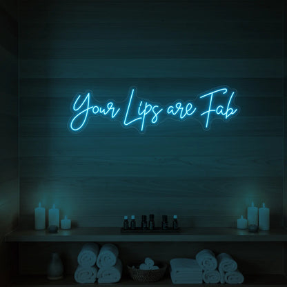 Photo of the 'Your Lips Are Fab' neon sign glowing in ice blue against a styled interior wall.