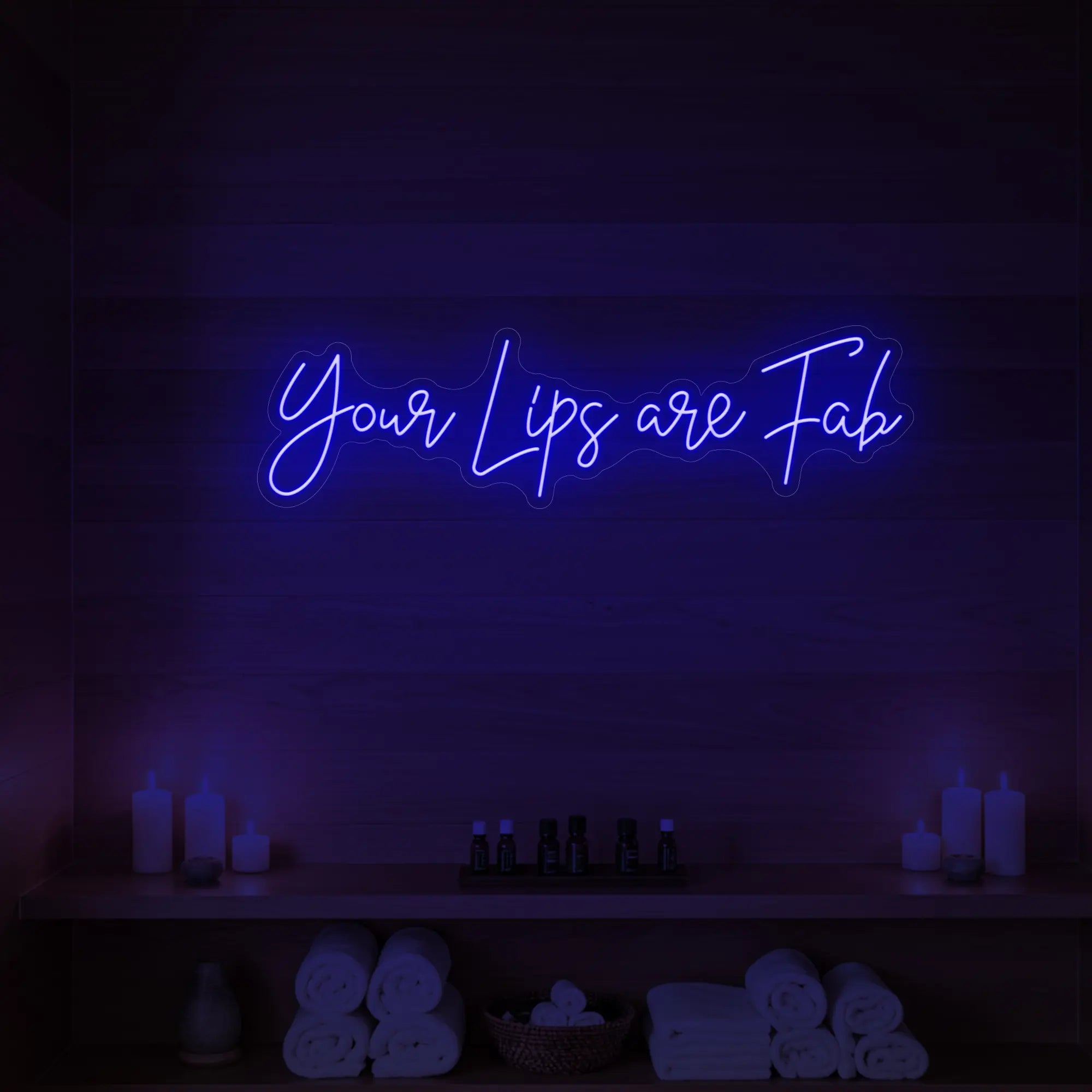 Photo of the 'Your Lips Are Fab' neon sign glowing in deep blue against a styled interior wall.