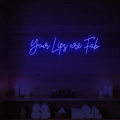 Photo of the 'Your Lips Are Fab' neon sign glowing in deep blue against a styled interior wall.