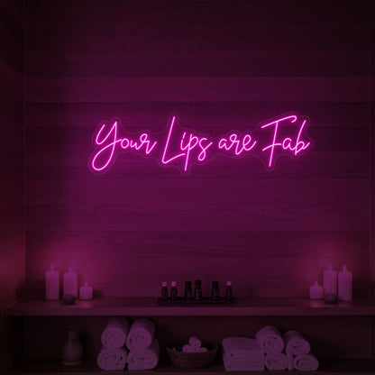 Photo of the 'Your Lips Are Fab' neon sign glowing in light pink against a styled interior wall.