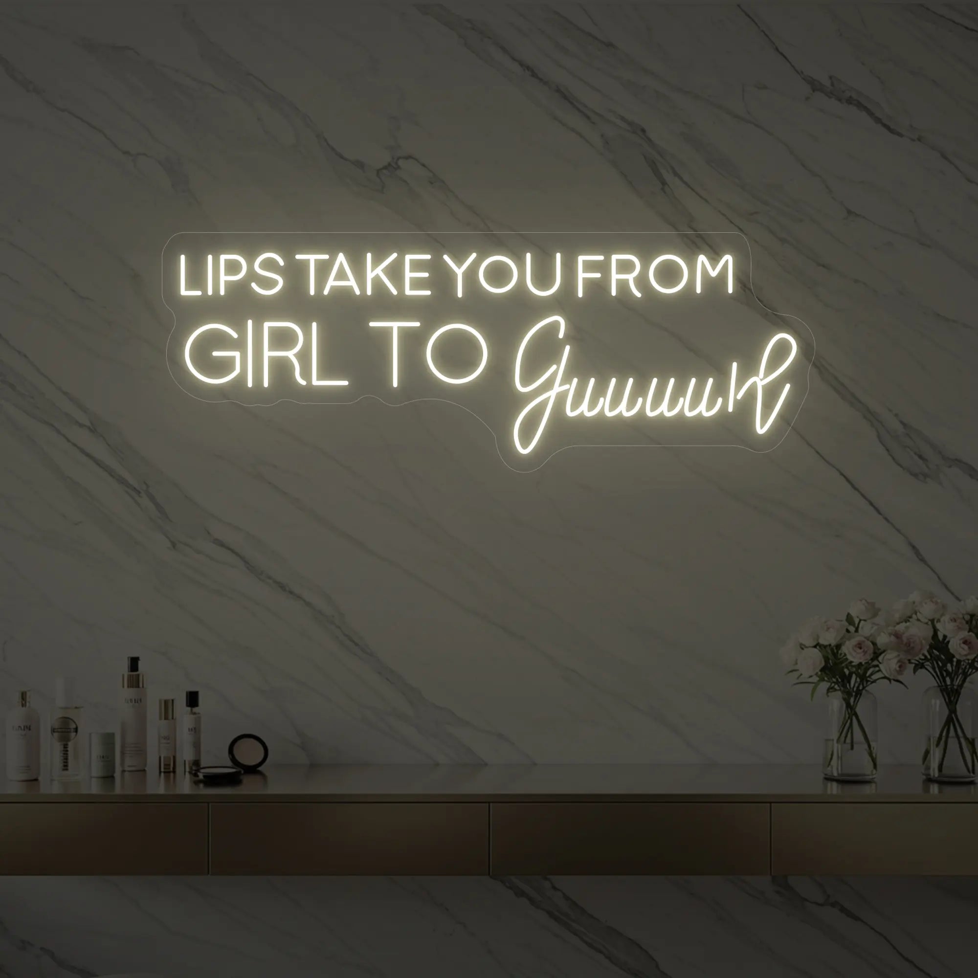 Photo of the 'LIPS TAKE YOU FROM GIRL TO Guuuurl' neon sign glowing in warm white against a styled interior wall.
