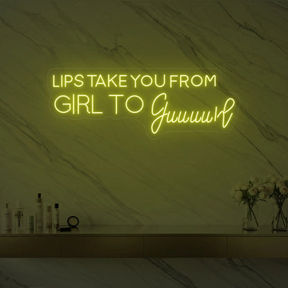 Photo of the 'LIPS TAKE YOU FROM GIRL TO Guuuurl' neon sign glowing in lemon yellow against a styled interior wall.